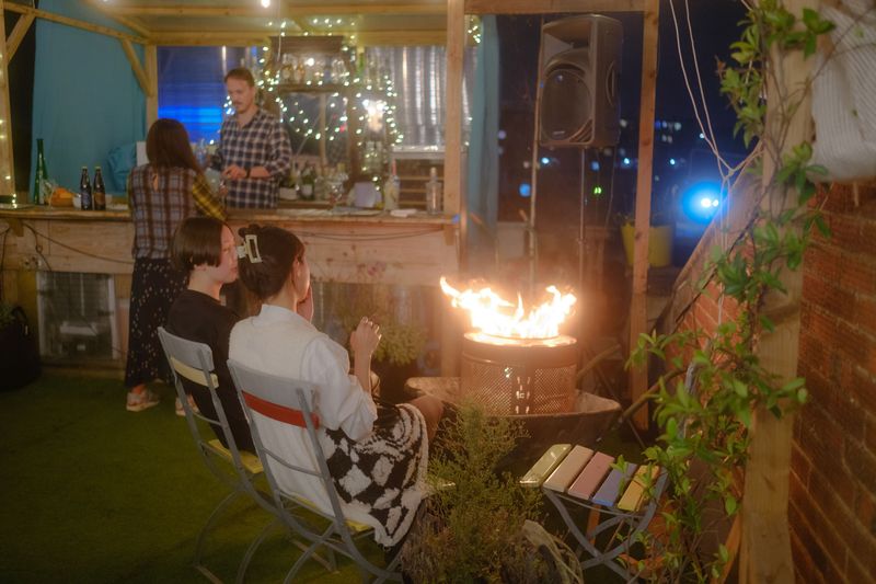 Guests sitting by the fire at Queensrollahouse roof terrace during Supper Club